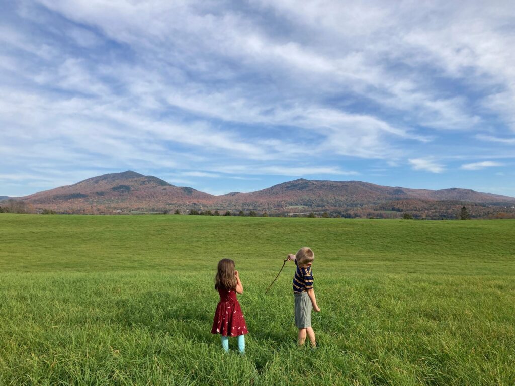 Two children exploring a grassy field with Vermont mountains in the background during a Field, Farm & Forest outdoor learning day