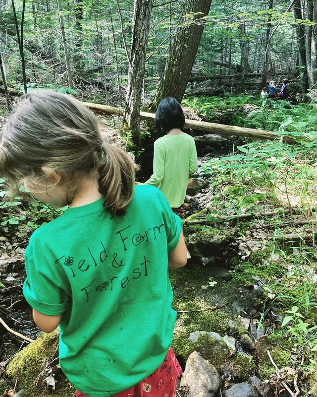 A child wearing a green Field, Farm & Forest shirt in the forest